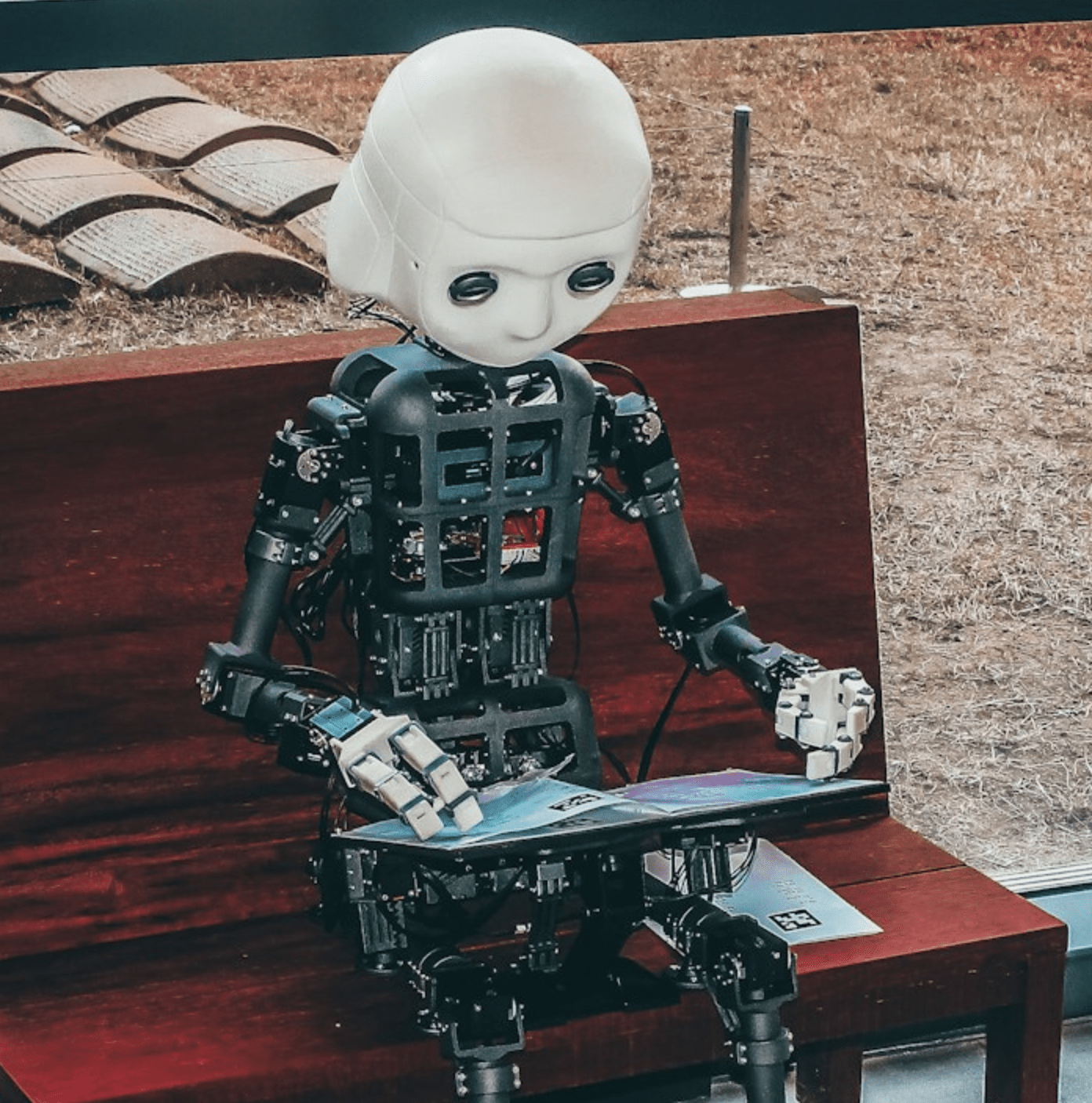 A robot working on a laptop while sitting on a bench.